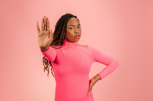 A portrait of a young African woman in pink against a pink background with the right hand stretched forward in a way to say no.