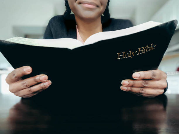Close-up cropped view of black woman reading bible at kitchen table