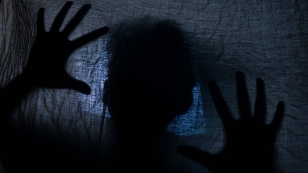Shadow silhouette of man trap under blanket with dim light for spooky footage to depict factors that fuel demon obsession