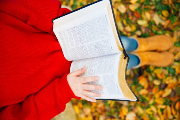 Little girl is sitting in the park covered with fallen leaves and reading the bible as a depiction of a reading plan won’t make you miss out