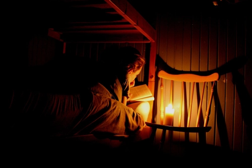A woman reading with candle light in the dark room to sign off dangers of overreliance on Bible reading plans