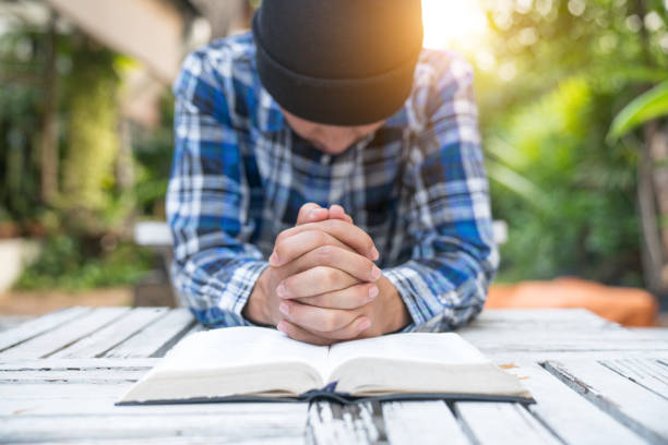 A man with hands in praying posture with a Bible on a wooden table before him, an illustration of expectation.