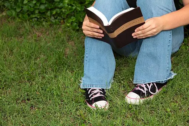 A half body of someone reading the Bible outdoors to illustrate encouragement