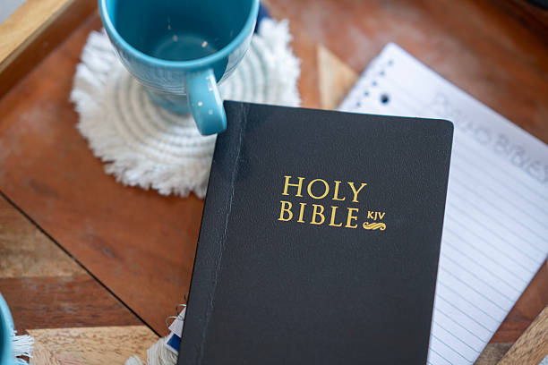A close-up view of a Bible with a notebook, and a blue coffee mug arranged on a wooden surface. 
