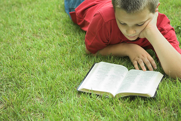Young boy keenly reading a Bible outside.