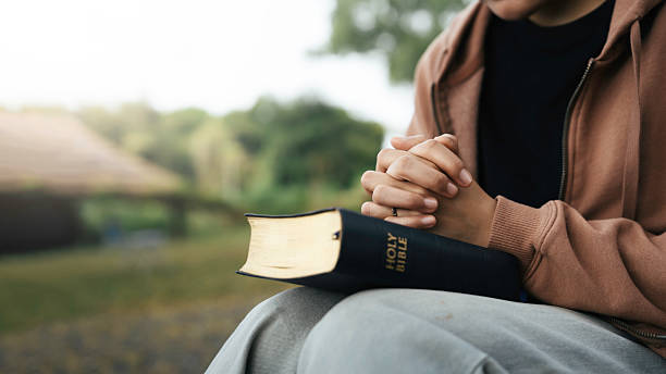 A you woman holding hands in prayer posture on a Bible to illustrate ways the gospels shape our Christian walk