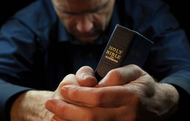 A Man praying holding a Holy Bible.